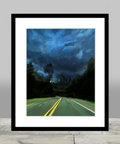 Sharp double yellow lines guide the viewer down a country road as a storm approaches.